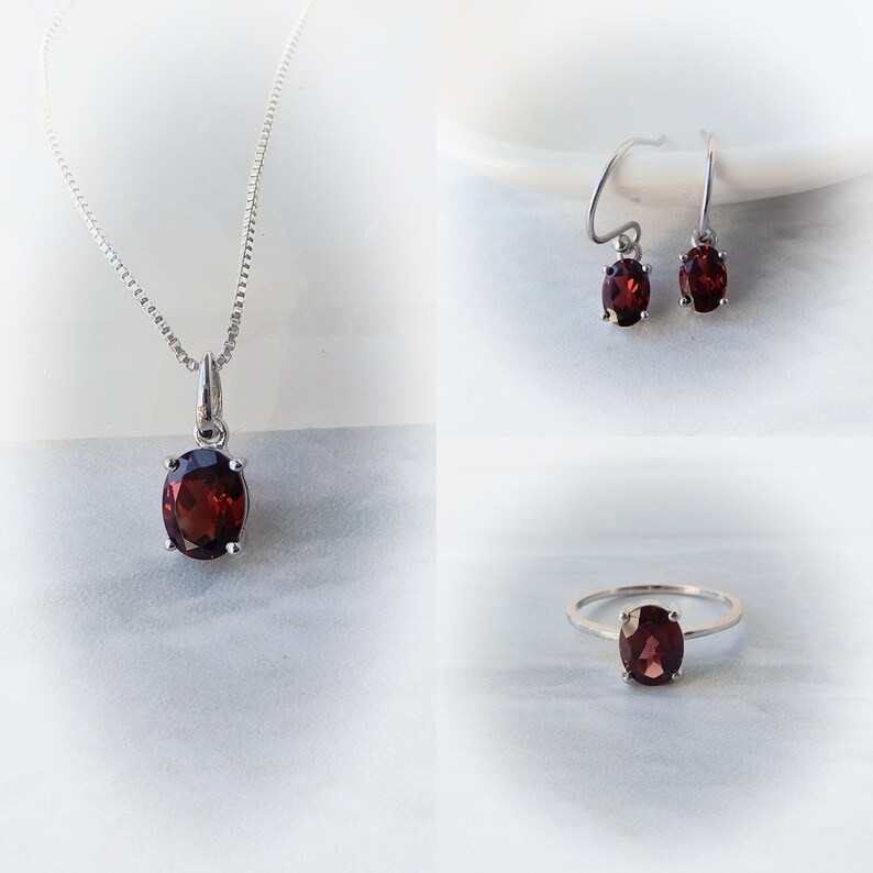 Pu&ograve; includere: Un set di gioielli in granato con una collana con ciondolo, orecchini e un anello. Ogni pezzo presenta una pietra preziosa di granato rosso di forma ovale incastonata in argento.