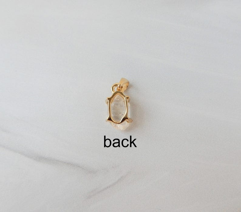 May include: A gold-coloured pendant with a clear, irregular-shaped stone. The pendant has a small loop at the top for a chain. The word "back" is printed below the pendant.