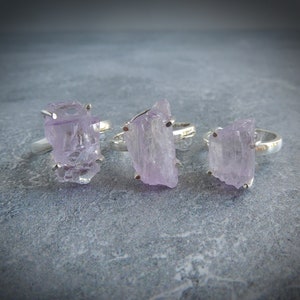 K&ouml;nnte beinhalten: Drei Silberringe mit rohen Amethyststeinen. Die Amethyststeine sind hellviolett und haben eine raue, nat&uuml;rliche Textur.