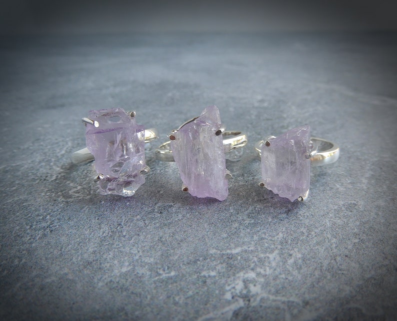 K&ouml;nnte beinhalten: Drei Silberringe mit rohen Amethyststeinen. Die Amethyststeine sind hellviolett und haben eine raue, nat&uuml;rliche Textur.