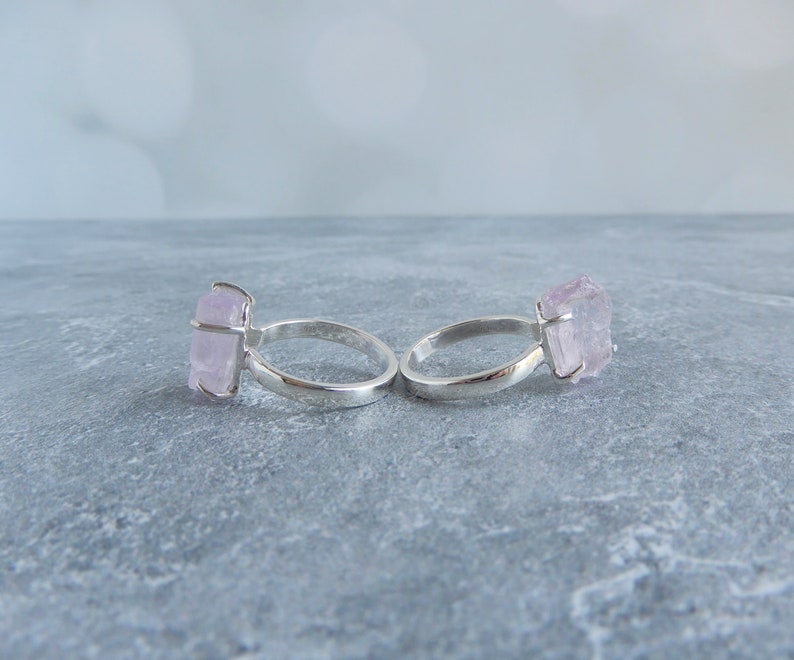 K&ouml;nnte beinhalten: Zwei silberne Ringe mit rosafarbenen Kristallsteinen. Die Ringe liegen auf einer grauen Oberfl&auml;che.