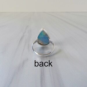 May include: A silver ring with a teardrop-shaped opal gemstone. The ring is shown from the back, with the setting visible.