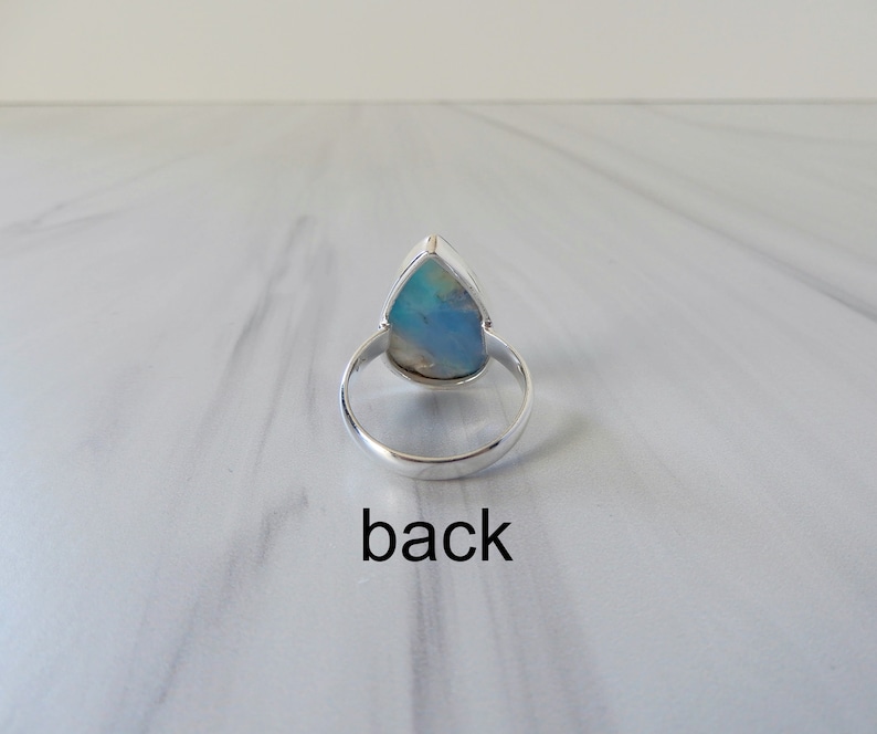 May include: A silver ring with a teardrop-shaped opal gemstone. The ring is shown from the back, with the setting visible.