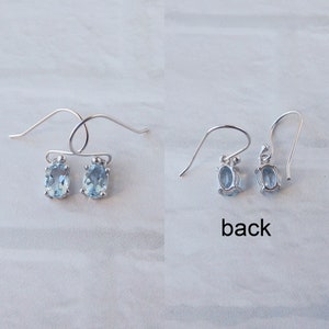 May include: A pair of silver earrings with oval-shaped light blue gemstones. The earrings have a simple design and are shown from the front and back.
