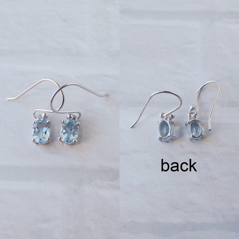 May include: A pair of silver earrings with oval-shaped light blue gemstones. The earrings have a simple design and are shown from the front and back.