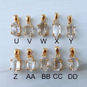 May include: Ten gold-coloured pendants featuring clear, raw crystal stones. Each pendant has a unique shape and is labelled with a letter from U to DD. The pendants are displayed on a light-coloured surface.
