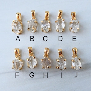 May include: Ten gold-coloured pendants, each featuring a raw, clear crystal stone. The pendants have irregular shapes and are suspended from small, gold-coloured bails. They are labelled A to J.