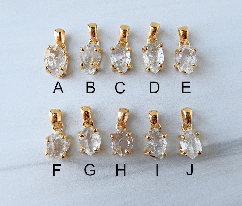 May include: Ten gold-coloured pendants, each featuring a raw, clear crystal stone. The pendants have irregular shapes and are suspended from small, gold-coloured bails. They are labelled A to J.
