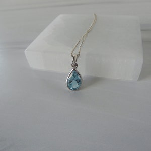 May include: A silver chain necklace with a teardrop-shaped blue topaz pendant.