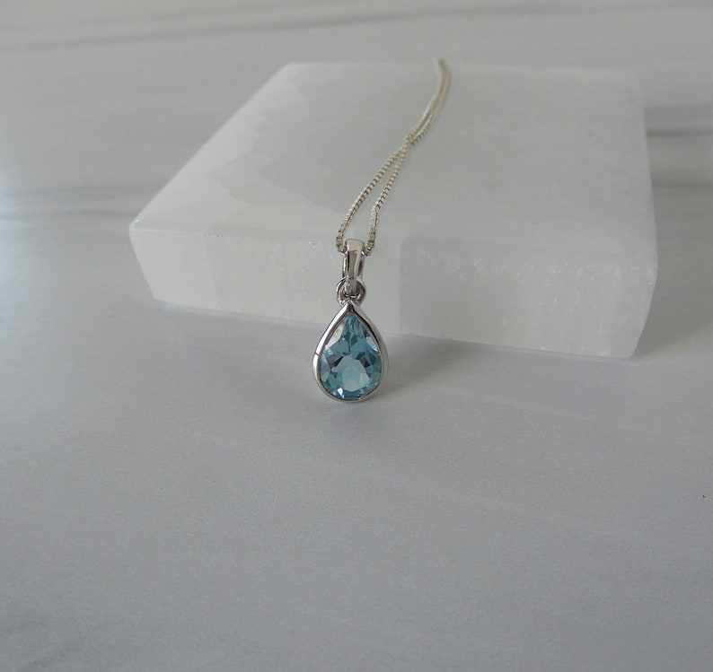 May include: A silver chain necklace with a teardrop-shaped blue topaz pendant.