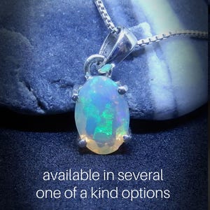 May include: A silver chain necklace with a pendant featuring a light blue oval opal gemstone. The opal has a green and blue iridescent sheen. The text "available in several one of a kind options" is below the pendant.