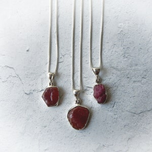 May include: Three silver necklaces with red gemstone pendants. The gemstones are irregularly shaped and have a rough, natural look.
