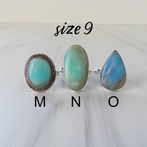 May include: Three silver rings with different colored gemstones. The ring on the left has a round, light blue gemstone with a silver border. The middle ring has an oval, light green gemstone. The ring on the right has a teardrop-shaped, light blue gemstone. The rings are labeled M, N, and O, respectively. The text "size 9" is above the rings.