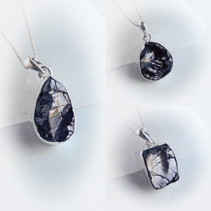 May include: Three silver necklaces with black gemstone pendants. The pendants are in different shapes, including a teardrop, a square, and a rectangle.