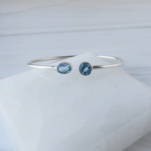 May include: A silver bangle bracelet with two oval-shaped blue topaz gemstones.