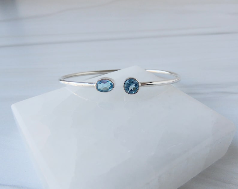May include: A silver bangle bracelet with two oval-shaped blue topaz gemstones.