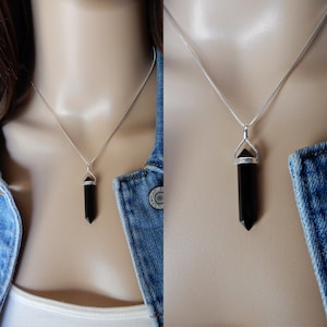 May include: A silver chain necklace with a black gemstone pendant in the shape of a point. The pendant is set in a silver bezel.