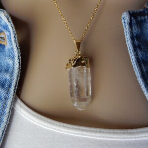 Puede incluir: Un collar de cadena dorada con un colgante de cristal de cuarzo transparente. El cristal est&aacute; envuelto en oro en la parte superior.