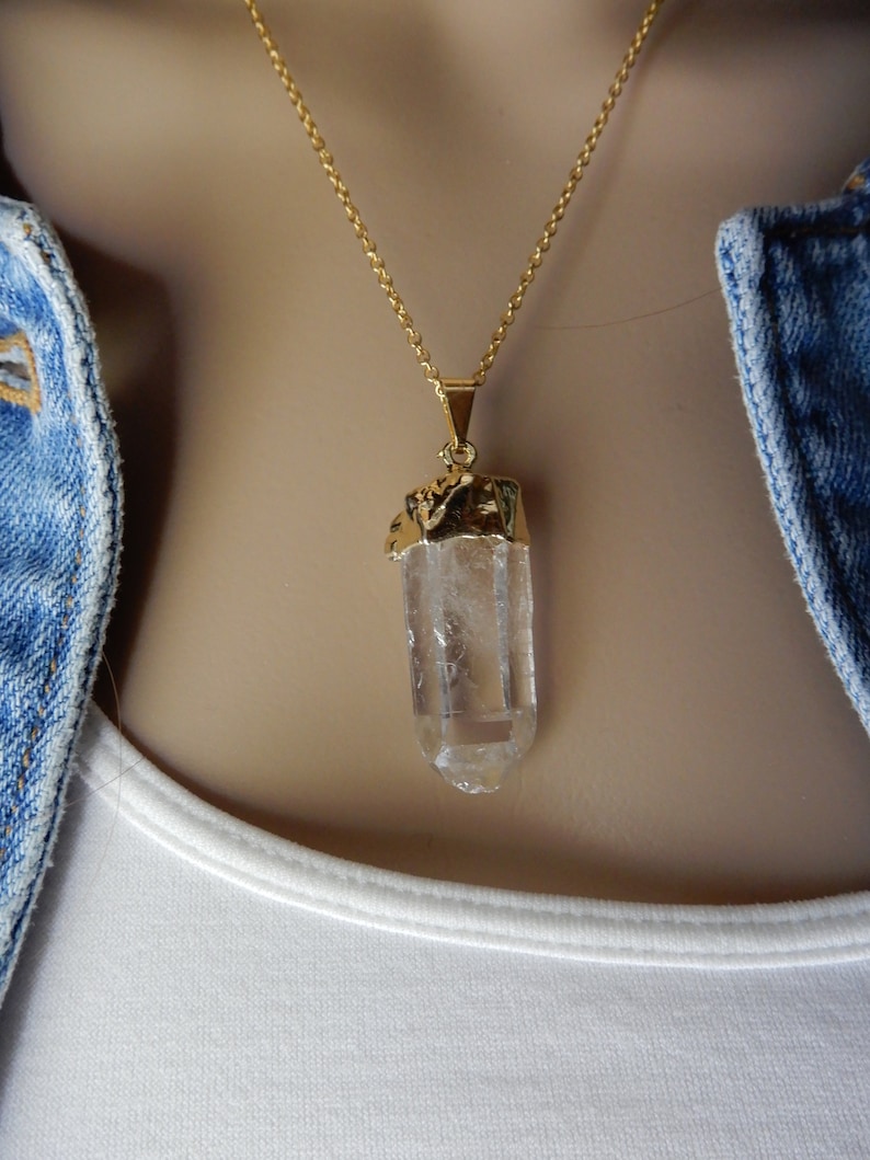 Puede incluir: Un collar de cadena dorada con un colgante de cristal de cuarzo transparente. El cristal est&aacute; envuelto en oro en la parte superior.