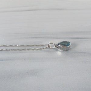 May include: A silver chain necklace with a teardrop-shaped blue gemstone pendant.
