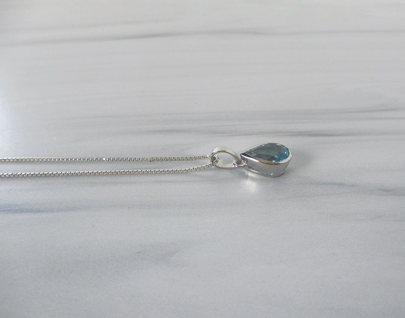 May include: A silver chain necklace with a teardrop-shaped blue gemstone pendant.