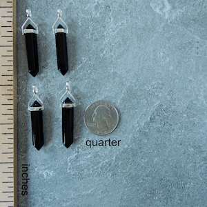 May include: Four black onyx crystal point pendants with silver bail settings. The pendants are approximately 1 inch long and are shown next to a US quarter for size comparison.  "quarter" is written below the coin.