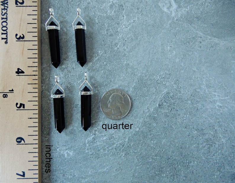 May include: Four black onyx crystal point pendants with silver bail settings. The pendants are approximately 1 inch long and are shown next to a US quarter for size comparison.  "quarter" is written below the coin.