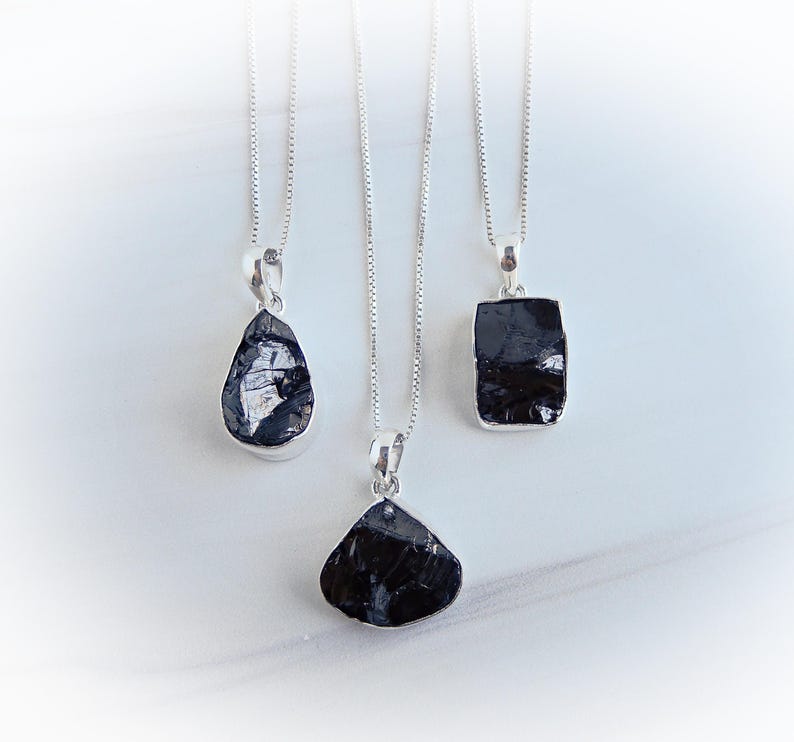 May include: Three silver necklaces with black gemstone pendants. The pendants are different shapes, including a teardrop, a square, and a triangle.