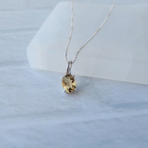 Peut inclure: Un collier en cha&icirc;ne argent avec un petit pendentif de forme ovale orn&eacute; d'une pierre pr&eacute;cieuse brun clair.