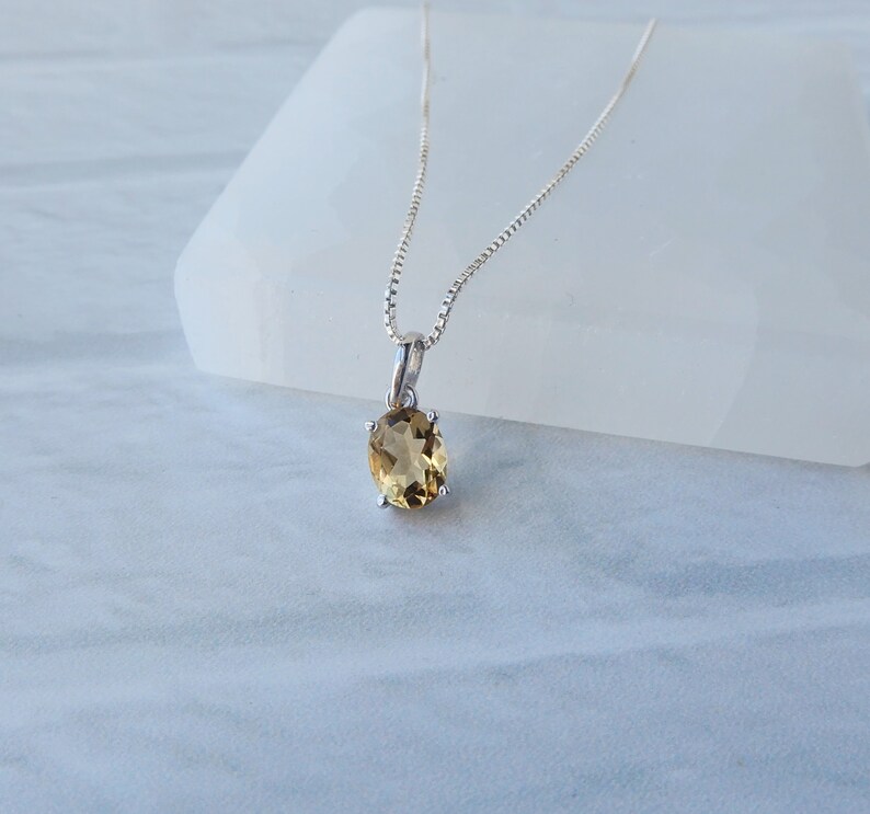 Peut inclure: Un collier en cha&icirc;ne argent avec un petit pendentif de forme ovale orn&eacute; d'une pierre pr&eacute;cieuse brun clair.