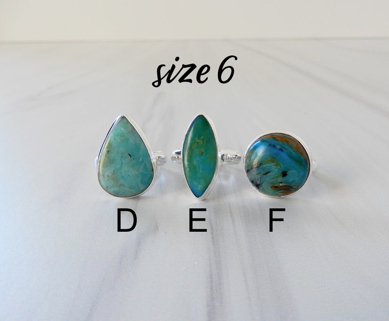 May include: Three silver rings with different turquoise gemstones. The rings are labeled D, E, and F. The text "size 6" is written above the rings.
