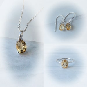 Peut inclure: Un ensemble de bijoux compos&eacute; d'un collier, de boucles d'oreilles et d'une bague en argent avec une pierre ovale brun clair.