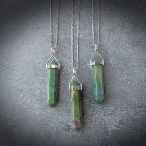 May include: Three silver chain necklaces with green and pink gemstone pendants in the shape of a point.