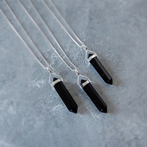 May include: Three silver necklaces with black crystal point pendants. The pendants are shaped like long, thin points.