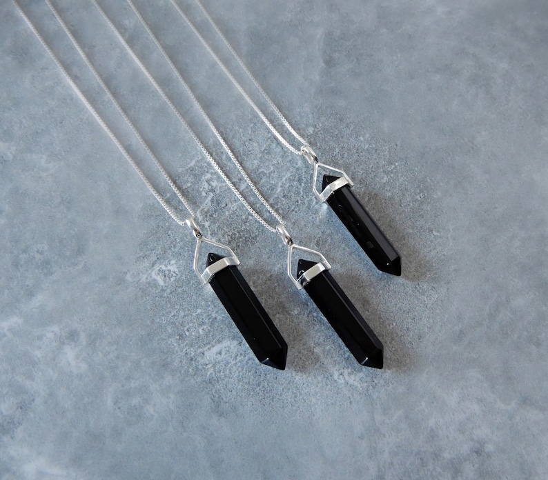 May include: Three silver necklaces with black crystal point pendants. The pendants are shaped like long, thin points.