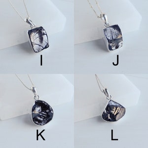 May include: Four silver necklaces with black gemstone pendants. The pendants are in different shapes, including square, rectangular, and teardrop. The necklaces are on a white background.