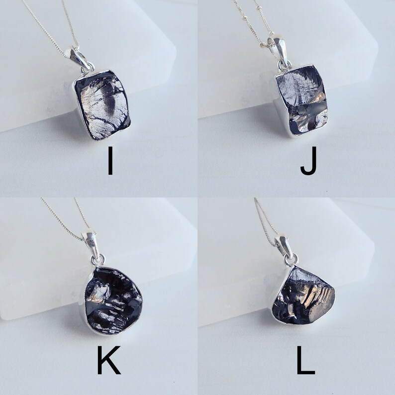 May include: Four silver necklaces with black gemstone pendants. The pendants are in different shapes, including square, rectangular, and teardrop. The necklaces are on a white background.