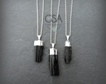 Peut inclure: Trois colliers avec pendentifs en tourmaline noire, avec des capuchons et des chaînes en métal argenté. Les colliers sont présentés sur une surface gris foncé. L'image comprend le texte "CSA Gemstone appeal".