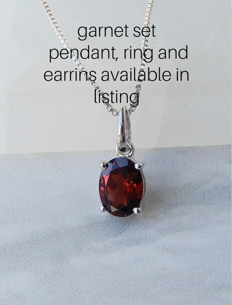 Pu&ograve; includere: Una collana con catena d'argento con un ciondolo con una pietra di granato rossa. Il testo "garnet set pendant, ring and earrings available in listing" &egrave; visibile sopra il ciondolo.