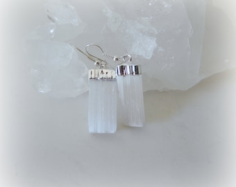 Puede incluir: Un par de pendientes de plata con colgantes de cristal de selenita blanca. Los cristales son de forma rectangular y tienen una textura estriada.