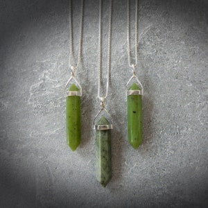 May include: Three silver necklaces with green jade stone pendants in the shape of a point. The pendants are all the same size and shape, but the chains are different lengths.