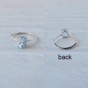 May include: A silver ring with a light blue oval gemstone. The ring is shown from the front and back.