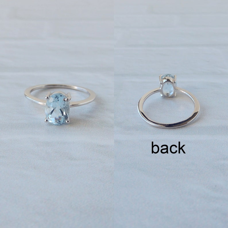 May include: A silver ring with a light blue oval gemstone. The ring is shown from the front and back.