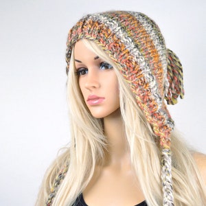 May include: A crocheted beanie with long, braided tassels in shades of orange, brown, and white. The beanie is worn by a mannequin with long blonde hair.