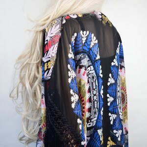 May include: Black sheer kimono with a colorful floral and geometric pattern. The kimono has black fringe trim on the sleeves.