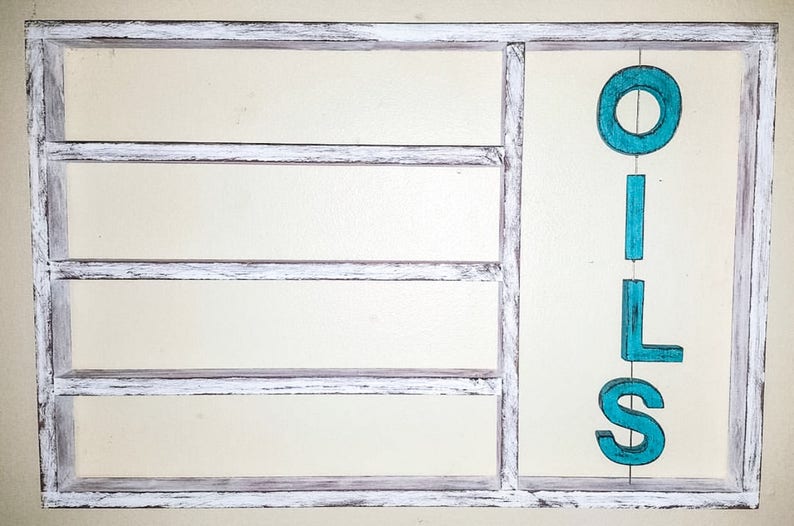 Puede incluir: Un estante de madera con marco blanco con cuatro compartimentos y la palabra "OILS" en letras turquesas. El marco tiene un aspecto envejecido y r&uacute;stico.