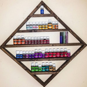 May include: A wooden diamond-shaped shelf unit with four shelves, displaying rows of small glass bottles with white caps. The bottles are filled with colorful liquids, and there are two taller bottles on the top shelf.