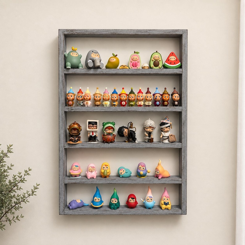 May include: A rectangular grey wooden wall shelf with five horizontal tiers displaying a collection of small, colourful, stylised character figurines. The figures vary in shape, including fruit-themed designs, humanoids, and diverse whimsical creatures.