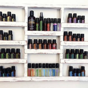 May include: White wooden shelf unit with multiple shelves, each filled with small glass bottles of essential oils. The bottles are arranged in rows and are labeled with different names. The shelf unit is a great way to store and display essential oils.