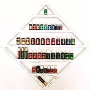 May include: A white diamond-shaped shelf with multiple shelves holding small glass bottles of essential oils. The bottles are arranged in rows and are various colours, including green, blue, red, and yellow. There are also two roll-on bottles on the bottom shelf.